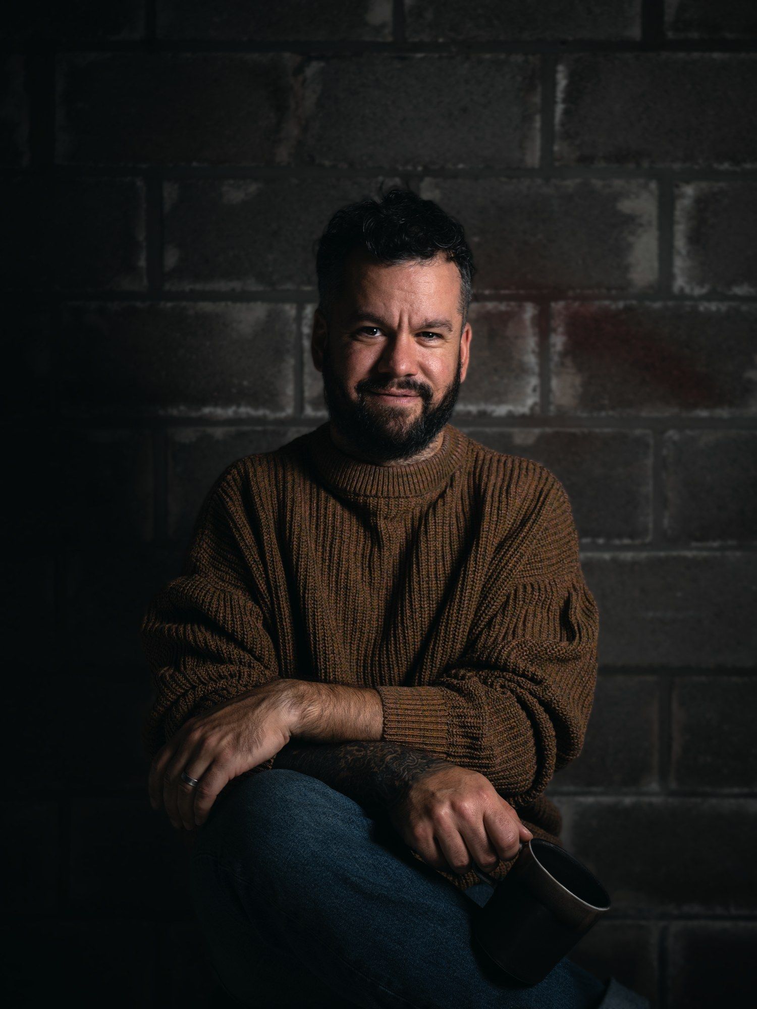 Portrait photo of Jochen, the 3D artist behind DRIMENSI, seated against a brick wall in a brown knit sweater